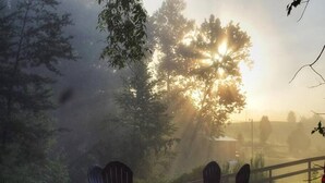 A serene outdoor seating area with Adirondack chairs and a table, surrounded by trees and a wooden fence. - Scenic Sunset Cabin RRG | Central | Hot Tub | Pets (Campton)