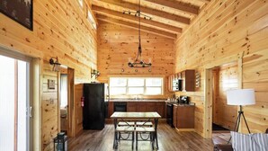 A wooden cabin interior with a dining table, benches, a kitchen area, and a living space with a sofa. - Scenic Sunset Cabin RRG | Central | Hot Tub | Pets (Campton)