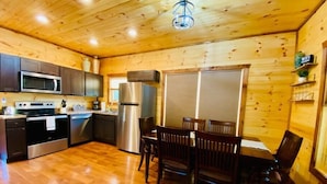 A wooden cabin interior with a kitchen, dining area, and a ceiling light fixture.