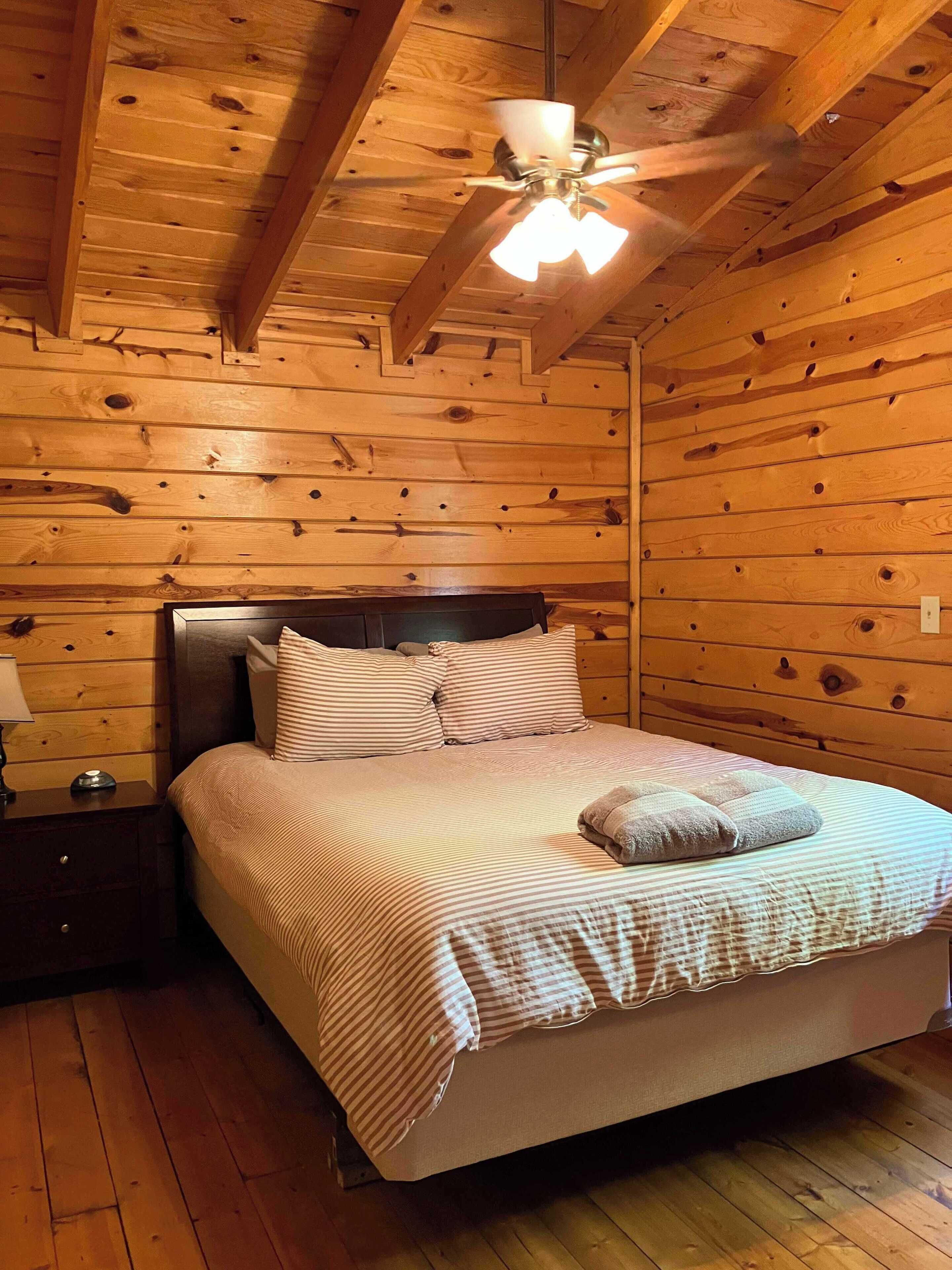 Ein Schlafzimmer einer Holzhütte mit Bett, Nachttisch und Deckenventilator.
