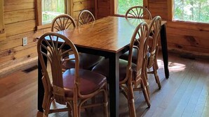 Une cabane en bois avec une table et des chaises, de grandes fenêtres et un luminaire suspendu.