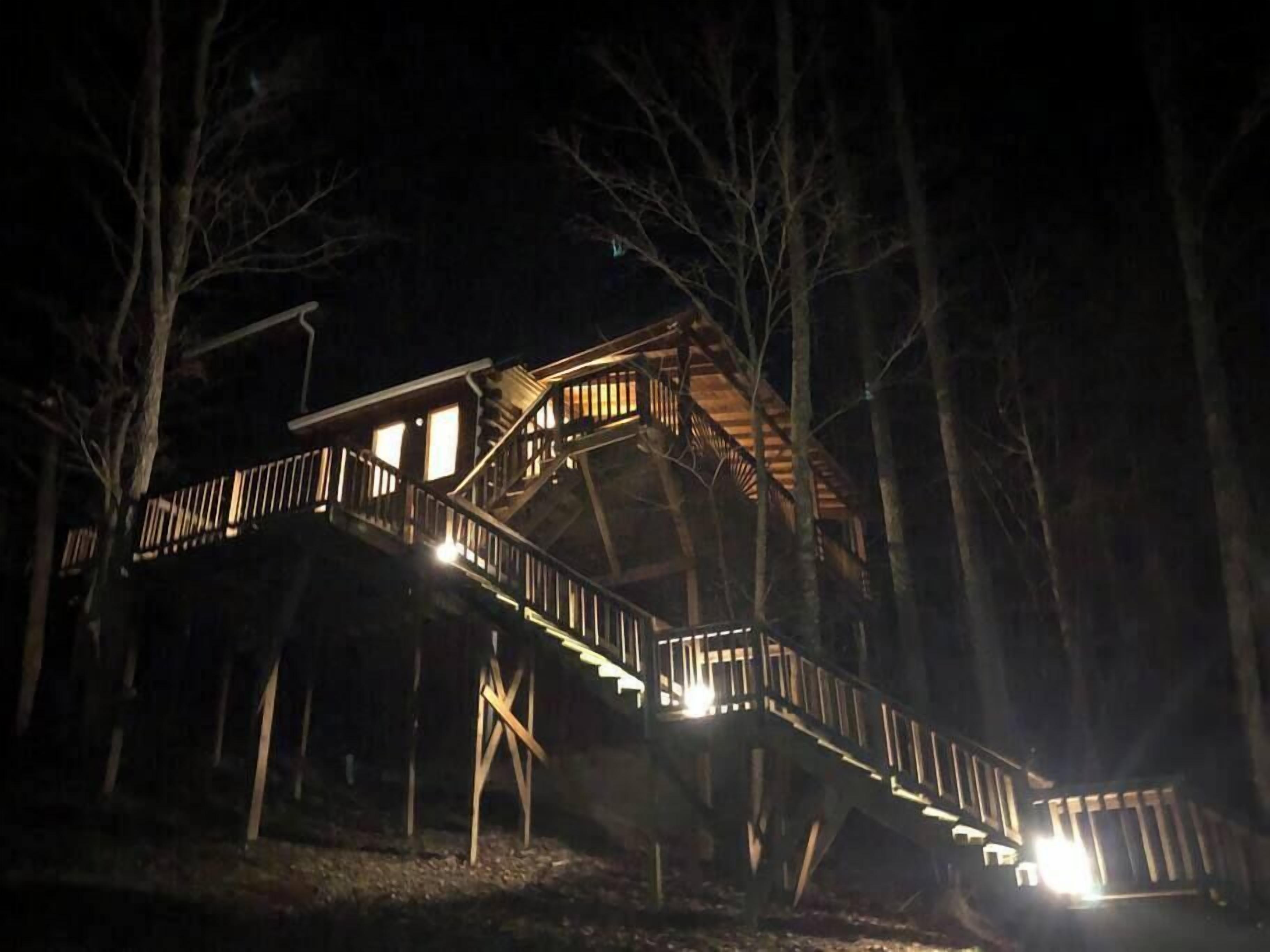 A wooden cabin with a staircase leading to a deck, surrounded by trees.