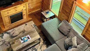 L’intérieur d’un chalet en bois, avec un canapé, un téléviseur, une petite table et une fenêtre.