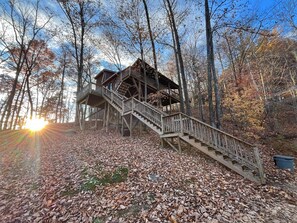 Une cabane en bois avec un escalier menant à une terrasse entourée d’arbres.