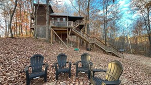 Une cabane dotée d’une terrasse en bois et d’un escalier menant à un balcon, entourée d’arbres et recouverte de feuilles mortes.