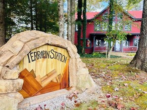 A rustic stone archway with the text "TERRAPIN STATION" and a wooden door, leading to a red building with a porch.