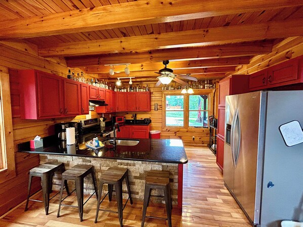 A wooden cabin kitchen with a central island, red cabinets, a stainless steel refrigerator, and a stone wall.