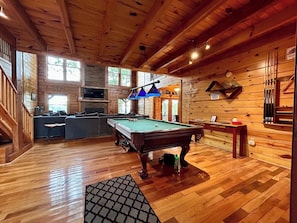 A wooden cabin interior with a pool table, a sofa, and a billiards table.