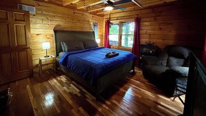 Ein Schlafzimmer einer Holzhütte mit einem Bett, einem Sessel, einem Nachttisch und einem Deckenventilator.