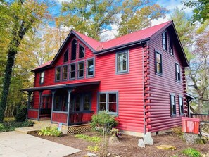 A red log cabin with a porch, multiple windows, and a chimney.