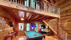 Ein Holzinnenraum mit Poolbillard, Billardtisch und einer Treppe zu einer oberen Ebene.