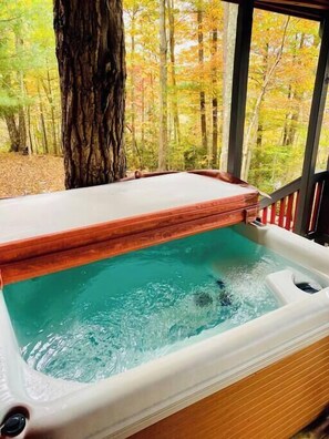 A hot tub with a wooden edge, surrounded by a wooden deck and a glass window.