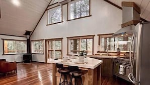 A spacious kitchen with a large island, wooden flooring, and a high ceiling with exposed beams. - The Founder - Iconic Rockhouse Cabin! (Campton)