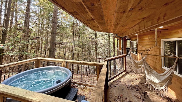 A wooden deck with a hot tub, hammock, and a view of the forest. - The Founder - Iconic Rockhouse Cabin! (Campton)