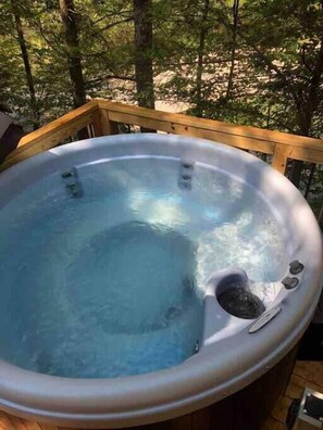 A hot tub on a wooden deck surrounded by trees.