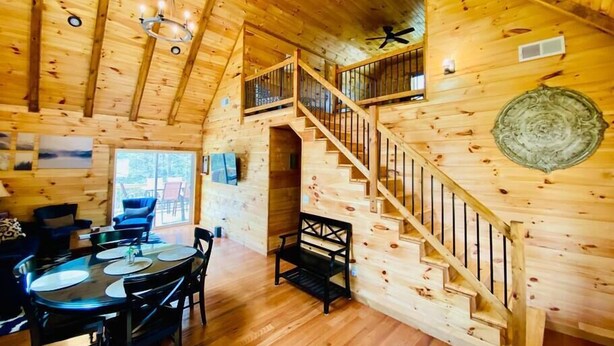 A wooden cabin interior with a dining area, staircase, and a ceiling fan.