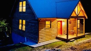 A log cabin with a blue roof, a front porch with a bench, and a visible door.