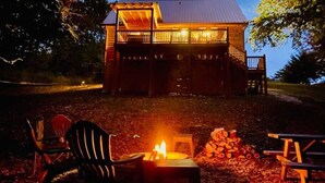 A cabin with a wooden exterior, a balcony, and a fire pit in front.