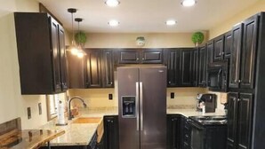 A modern kitchen with dark cabinets, stainless steel appliances, a wooden bar counter, and a zebra-patterned rug. - Walden’s Wonder – Artful Cabin w/ Valley View (Pine Ridge, KY)