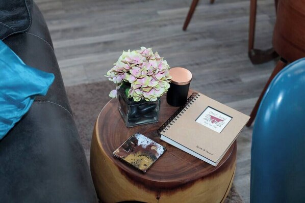 A small wooden side table with a notebook, a coffee cup, a vase with flowers, and a small decorative item.