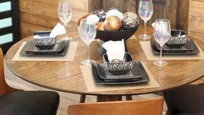 A round dining table with black and white patterned placemats, a central bowl with fruits and a napkin, and two wine glasses. - Walden’s Wonder – Artful Cabin w/ Valley View (Pine Ridge, KY)