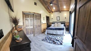 A bedroom with a bed, wooden wardrobe, ceiling fan, and a decorative plant. - Walden’s Wonder – Artful Cabin w/ Valley View (Pine Ridge, KY)