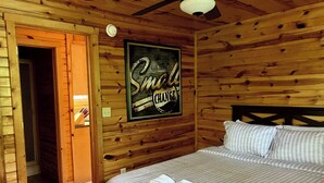 A wooden cabin room with a bed, a framed sign on the wall, and a door leading to another room. - Wildcat Cabin • Pet Friendly, Hot Tub, Forest Stay (Stanton)