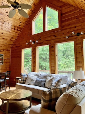 Relax in this cabin with a high ceiling, comfortable sofa, and large windows offering a view of the surrounding greenery.