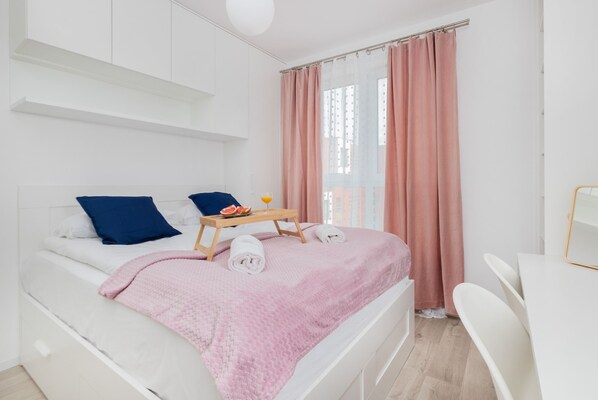 A modern bedroom with a bed, pillows, a bedside table with a tray, and a window with curtains.