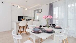 A modern kitchen with white cabinets, a microwave, and a sink. There is a dining area with white chairs and a table set for two with pink and blue plates.