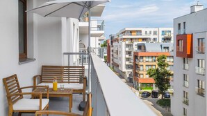 A balcony with wooden furniture and a bottle of orange juice, overlooking a row of modern buildings.
