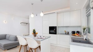 A modern kitchen with white cabinets, a central island with bar stools, a built-in oven, and a large window.