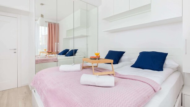 A modern bedroom with a large bed, a bedside table with a tray, and a mirror reflecting the room.