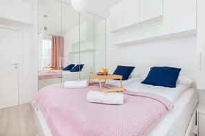 A modern bedroom with a large bed, a bedside table with a tray, and a mirror reflecting the room.