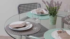 Une table dressée avec des assiettes, des couverts et des verres à vin, agrémentée d’une plante en pot.