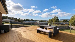 Une terrasse en bois avec des meubles d’extérieur, une vue sur un terrain de sport et un ciel dégagé.