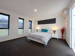 A bedroom with a bed, two bedside tables, a wall-mounted air conditioner, and large windows. - Spacious Family Retreat in Granton (Granton)