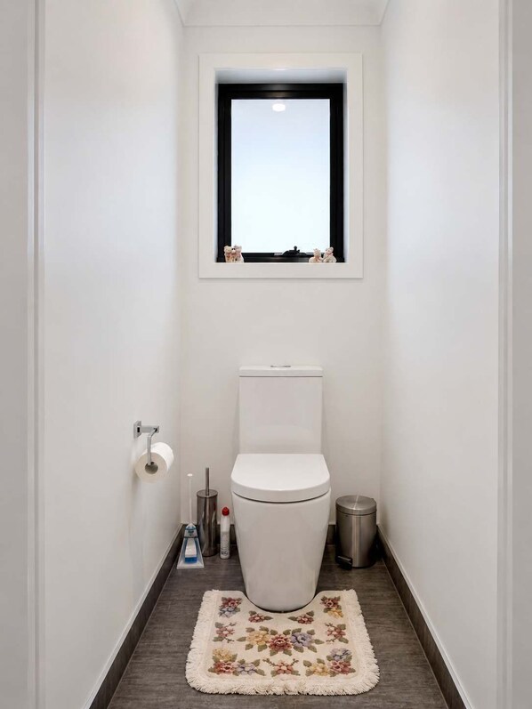 A narrow bathroom with a toilet, a small window, a trash bin, and a toilet paper holder. - Spacious Family Retreat in Granton (Granton)