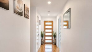 Un couloir avec un plancher en bois, des murs blancs et une porte en bois au fond.