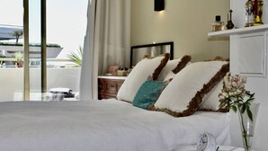 A bedroom with a large bed, a bedside table with a clock, and a view of the outside.