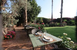 An outdoor dining area with tables set for two, surrounded by lush greenery and flowering plants. - Jnane Leila (Marrakech)