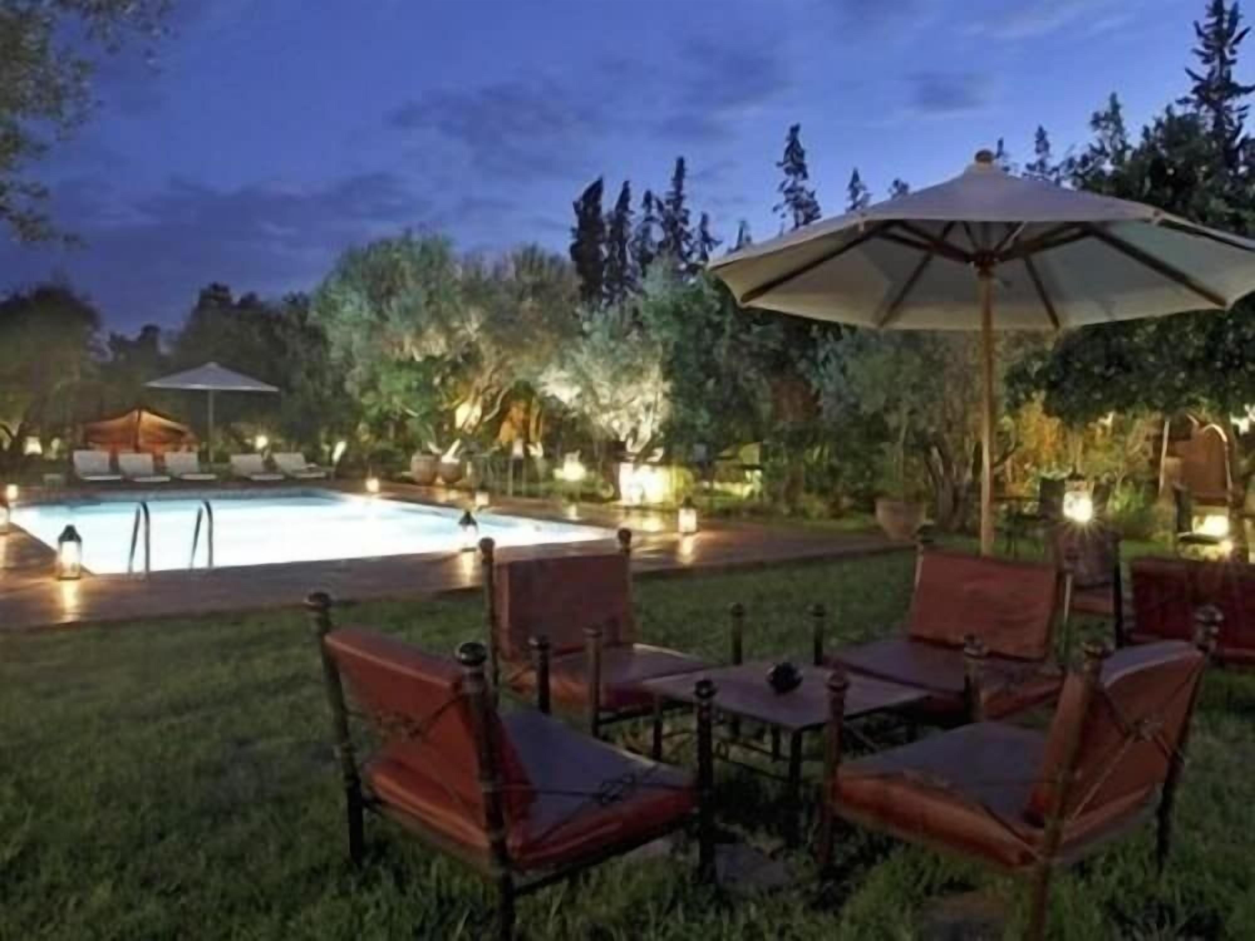 Un área de piscina al aire libre con sillones de descanso y sombrillas, rodeada de árboles y vegetación.