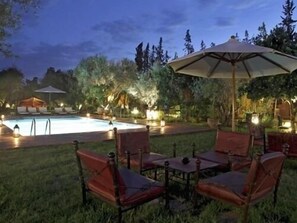 Un espace extérieur avec une piscine, des chaises longues et des parasols, le tout entouré d’arbres et de végétation.