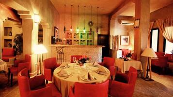 A restaurant with round tables set for dining, red chairs, and a brick wall backdrop.