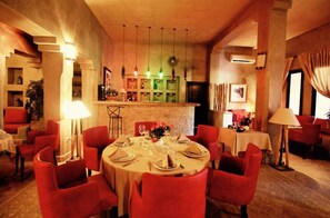 Un ristorante con tavoli rotondi apparecchiati per la cena, sedie rosse e una parete di mattoni.