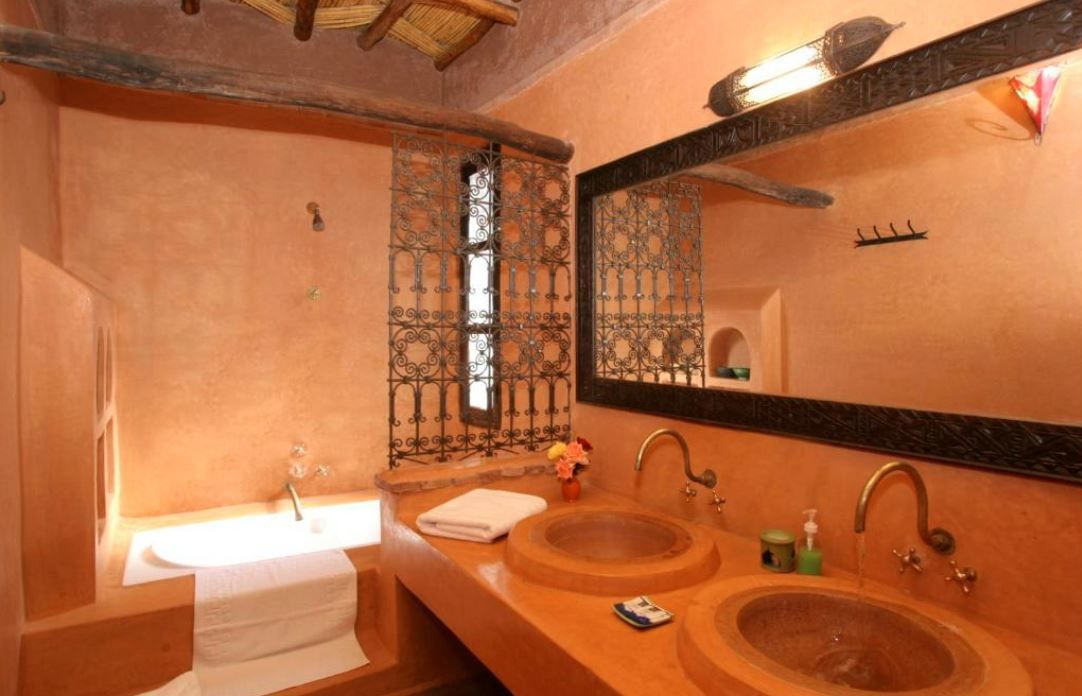 Un baño con un espejo grande, dos lavamanos y una ventana con rejas decorativas de hierro.