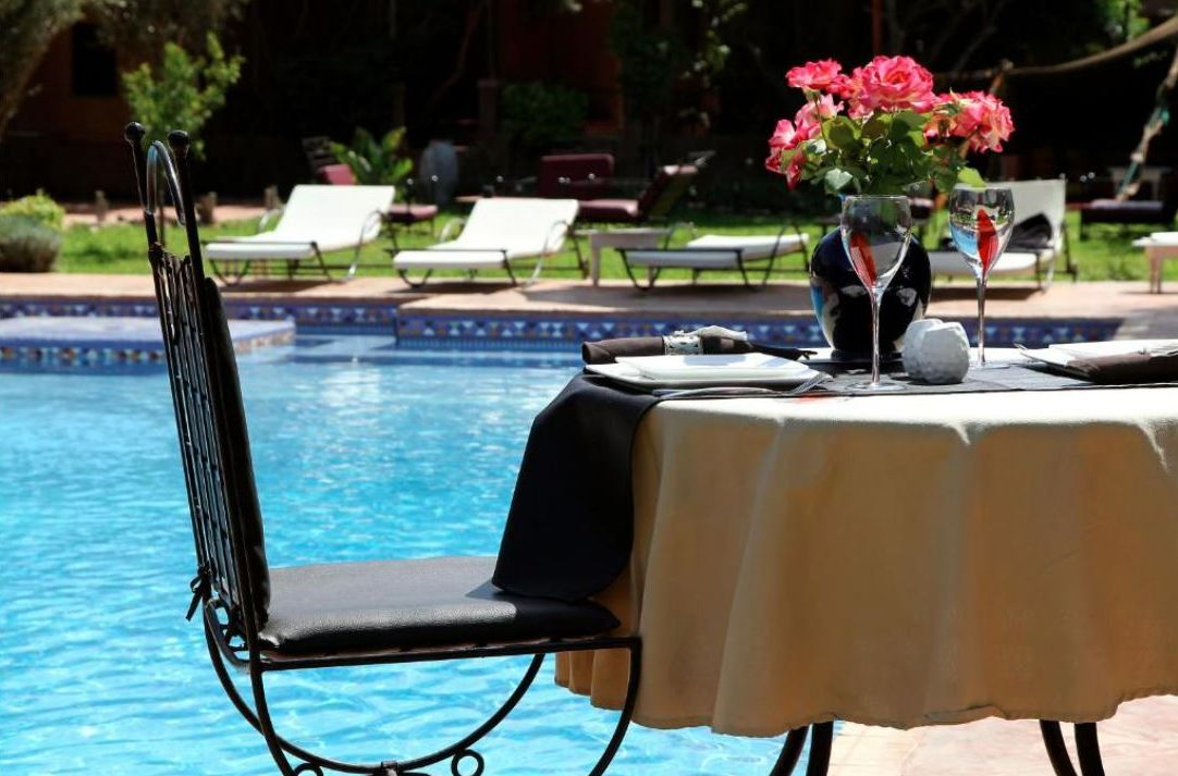 Ein Tisch am Pool mit einem Stuhl, einer Blumenvase und einem Glas Wasser.