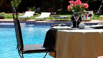 Ein Tisch am Pool mit einem Stuhl, einer Blumenvase und einem Glas Wasser.