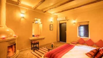 Un dormitorio acogedor con chimenea, una cama con ropa de cama roja y una mesita con un jarrón.