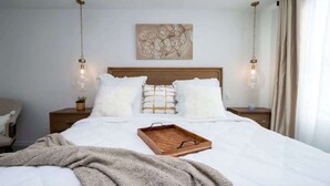 Ein ordentlich bezogenes Bett mit einem hölzernen Tablett, Kissen, einem Wandbild und zwei Nachttischlampen.